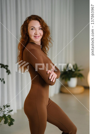 Woman poses in a brown outfit in a room with soft lighting and plants during a photoshoot Woman poses in a brown outfit in a room with soft lighting and plants during a photoshoot 137863967