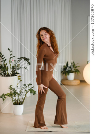Model poses indoors in a well-lit room surrounded by plants and soft decor while dressed in a brown outfit during a morning photoshoot focused on fashion and style 137863970