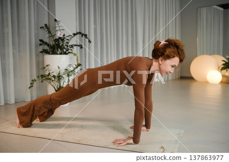 Yoga session takes place indoors in a studio with soft lighting, featuring a woman doing a plank position on a mat while surrounded by plants and soft-glow lamps Yoga session takes place indoors in a studio with soft lighting, featuring a woman doing a plank position on a mat while surrounded by plants and soft-glow lamps 137863977