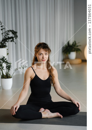 Woman practices yoga in a quiet studio with plants and soft lighting during a morning session focusing on mindfulness and relaxation Woman practices yoga in a quiet studio with plants and soft lighting during a morning session focusing on mindfulness and relaxation 137864031