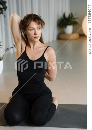 Woman stretches in a serene indoor space with plants while practicing yoga at a wellness studio during daylight hours 137864043
