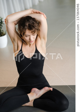 Woman stretches in a serene indoor space with plants while practicing yoga at a wellness studio during daylight hours 137864046
