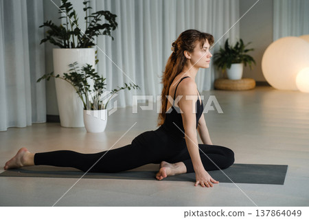 Yoga practice in a studio with plants and soft lighting during the morning hours featuring a woman in a stretching pose on a mat Yoga practice in a studio with plants and soft lighting during the morning hours featuring a woman in a stretching pose on a mat 137864049