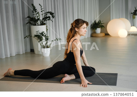 Yoga practice in a studio with plants and soft lighting during the morning hours featuring a woman in a stretching pose on a mat Yoga practice in a studio with plants and soft lighting during the morning hours featuring a woman in a stretching pose on a mat 137864051