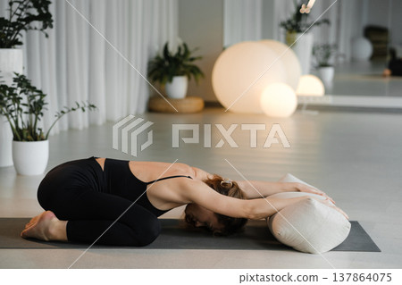 Woman practicing yoga in a bright studio during midday with calming decor and soft lights enhancing focus on relaxation and deep stretching Woman practicing yoga in a bright studio during midday with calming decor and soft lights enhancing focus on relaxation and deep stretching 137864075