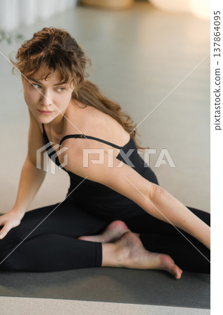 Woman practicing yoga at home during day in a peaceful setting with plants and soft lighting 137864095