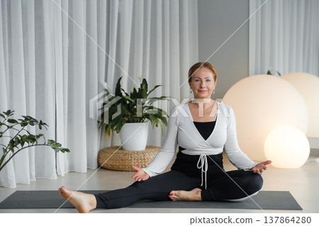 Yoga session at home with a woman practicing in a quiet room during daylight near plants and soft lighting Yoga session at home with a woman practicing in a quiet room during daylight near plants and soft lighting 137864280