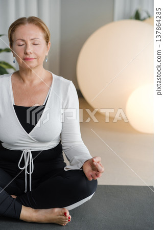 Woman practices meditation in a calm studio space with soft lighting and large round lights in the background during a wellness session focused on relaxation and mindfulness Woman practices meditation in a calm studio space with soft lighting and large round lights in the background during a wellness session focused on relaxation and mindfulness 137864285