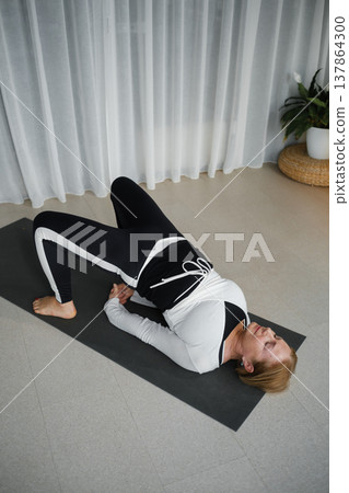 Woman practices yoga in a bright indoor space during morning hours with natural light streaming through sheer curtains Woman practices yoga in a bright indoor space during morning hours with natural light streaming through sheer curtains 137864300