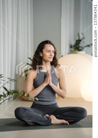 Woman practices yoga in a studio with plants and round lights during a morning session focused on mindfulness and relaxation Woman practices yoga in a studio with plants and round lights during a morning session focused on mindfulness and relaxation 137864341