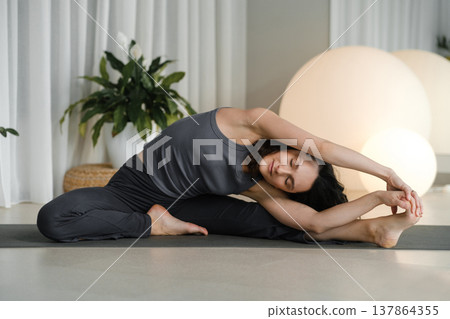 Woman practicing yoga in a modern studio during morning hours in front of soft lighting and plants 137864355