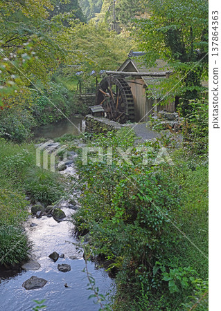 A beautiful watermill scene at Ishidatami Seiryuen in Uchiko Town, Ehime Prefecture. A pristine mountain village landscape adorned with a clear stream and lush greenery. A beautiful watermill scene at Ishidatami Seiryuen in Uchiko Town, Ehime Prefecture. A pristine mountain village landscape adorned with a clear stream and lush greenery. 137864363