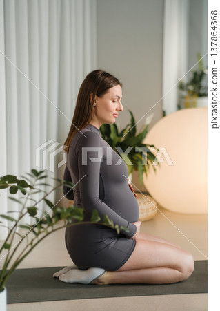 Pregnant woman practicing yoga in a calm indoor space with plants and soft lighting during evening hours Pregnant woman practicing yoga in a calm indoor space with plants and soft lighting during evening hours 137864368