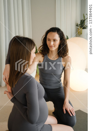 Two women practice yoga together in a bright indoor space with soft lighting in the morning, focusing on connection and support during pregnancy 137864401
