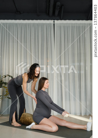 Pregnant woman stretches with instructor in modern studio during day 137864403