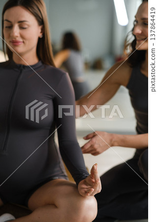 Yoga session for pregnant women in a studio setting with an instructor guiding a participant during a calm practice Yoga session for pregnant women in a studio setting with an instructor guiding a participant during a calm practice 137864419