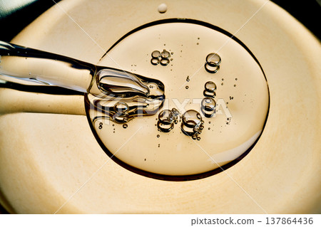 Pipette dripping golden serum with bubbles on surface Pipette dripping golden serum with bubbles on surface 137864436