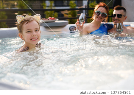 Family enjoys time together in hot tub during warm evening while city lights create a fun atmosphere Family enjoys time together in hot tub during warm evening while city lights create a fun atmosphere 137864561