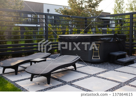 Hot tub area with lounge chairs in a backyard setting on a sunny day in a residential neighborhood surrounded by trees and a fence 137864615