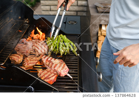 Outdoor grilling of meat and vegetables on a sunny day with family and friends gathered around the barbecue at a backyard barbecue party Outdoor grilling of meat and vegetables on a sunny day with family and friends gathered around the barbecue at a backyard barbecue party 137864628