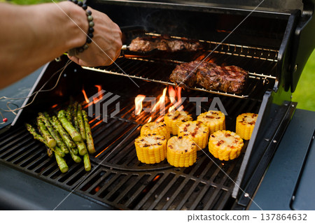 Grilling food on a barbecue with corn, asparagus, and steaks cooking outdoors during the day Grilling food on a barbecue with corn, asparagus, and steaks cooking outdoors during the day 137864632
