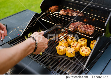 Grilling food on a barbecue with corn, asparagus, and steaks cooking outdoors during the day Grilling food on a barbecue with corn, asparagus, and steaks cooking outdoors during the day 137864633