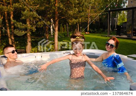 Family enjoys time in hot tub while child plays in water at home backyard on sunny day 137864674
