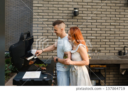 Couple enjoys grilling food and sharing drinks outdoors in a backyard setting on a sunny day Couple enjoys grilling food and sharing drinks outdoors in a backyard setting on a sunny day 137864719