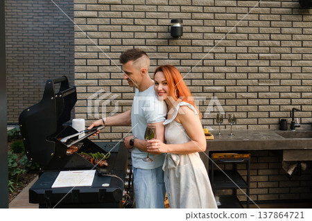 Couple enjoys grilling food and sharing drinks outdoors in a backyard setting on a sunny day 137864721