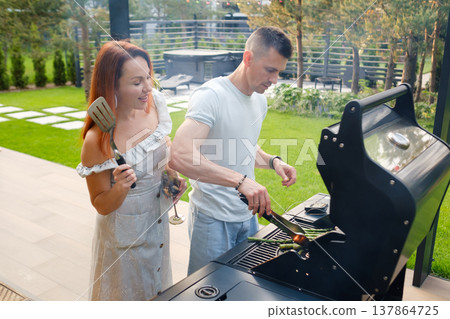 Friends cook on a grill in the backyard during a sunny day while enjoying drinks and having a good time with each other Friends cook on a grill in the backyard during a sunny day while enjoying drinks and having a good time with each other 137864725