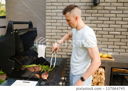 Cooking meat and vegetables on barbecue grill in backyard during sunny afternoon with friends nearby enjoying food and drinks Cooking meat and vegetables on barbecue grill in backyard during sunny afternoon with friends nearby enjoying food and drinks 137864745