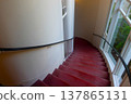 A corridor in a Western-style mansion with a spiral staircase covered in red carpet and large windows. 137865131