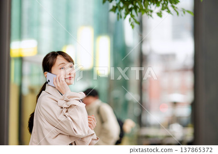 一位年輕的女商人正在街頭用手機打電話。 137865372