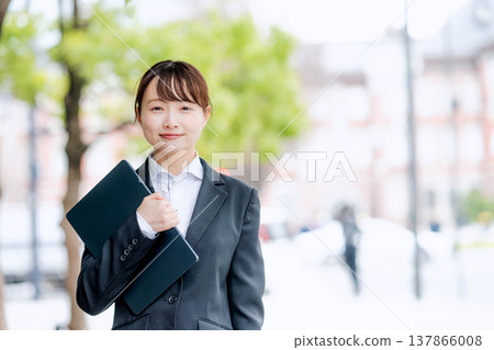 A young woman in a suit holding a laptop in one hand. A young woman in a suit holding a laptop in one hand. 137866008