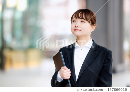 A young woman in a suit holding a laptop in one hand. A young woman in a suit holding a laptop in one hand. 137866016