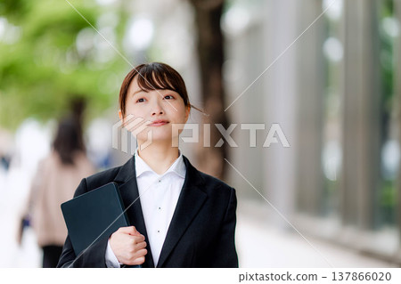 一位身穿西裝的年輕女子，一手拿著筆記型電腦。 137866020