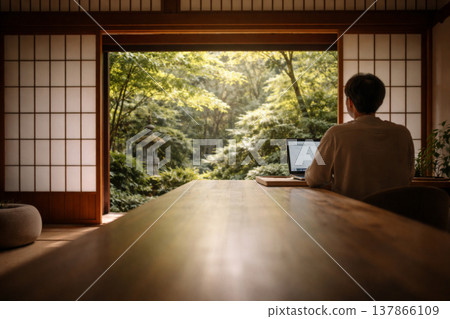 A man works remotely on his laptop in a Japanese-style room overlooking a Japanese garden. A man works remotely on his laptop in a Japanese-style room overlooking a Japanese garden. 137866109