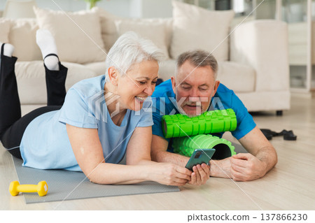 Yoga fitness training online. Senior couple practicing yoga fitness with online lessons on smartphone. Old wife husband watching training on phone before workout. Family doing sports exercise at home 137866230