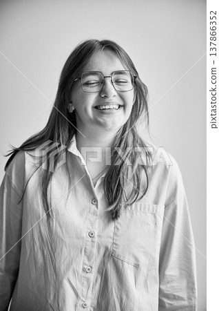 Portrait of beautiful girl smiling to camera. Cute girl in cream shirt and square glasses posing on white background. Black and white image. Portrait of beautiful girl smiling to camera. Cute girl in cream shirt and square glasses posing on white background. Black and white image. 137866352