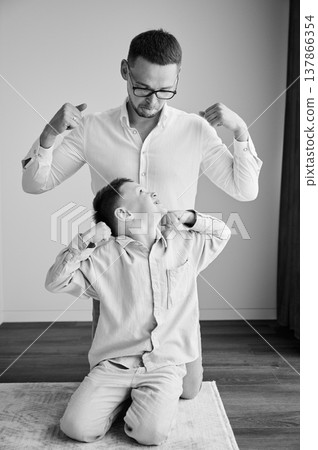 Young father playing with his curious son. Funny kid showing muscles to his dad. Family enjoying activity games at home. Black and white image. Young father playing with his curious son. Funny kid showing muscles to his dad. Family enjoying activity games at home. Black and white image. 137866354