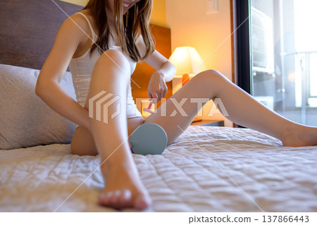 A young woman performs self-care on her VIO (vaginal, inner thigh) area, shaving with a razor while looking in a hand mirror. 137866443