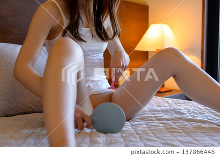 一位年輕女子正在對著手鏡進行私密處(陰道內側、大腿內側)的毛髮修剪。光線昏暗,她小心翼翼地修剪毛髮。 一位年輕女子正在對著手鏡進行私密處(陰道內側、大腿內側)的毛髮修剪。光線昏暗,她小心翼翼地修剪毛髮。 137866446