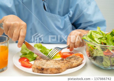 Asian elderly woman patient eating pork chop stake and vegetable salad for healthy food in hospital. Asian elderly woman patient eating pork chop stake and vegetable salad for healthy food in hospital. 137866742