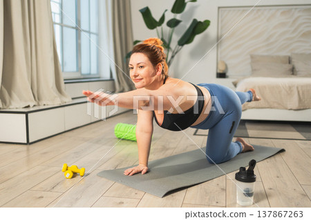 Yoga fitness workout training. Woman practicing yoga at home. Plus size female doing sports exercise on yoga mat indoor. Girl in sportswear have training workout for weight loss. Sport and fitness Yoga fitness workout training. Woman practicing yoga at home. Plus size female doing sports exercise on yoga mat indoor. Girl in sportswear have training workout for weight loss. Sport and fitness 137867263