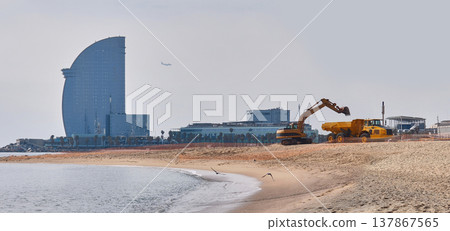 Beach restoration works in Barcelona with excavator and dump truck repairing sand on Mediterranean urban beach 137867565