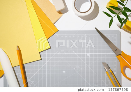 Workspace with cutting mat, scissors, cutter, yellow paper and stationery on white desk. Copyspace Workspace with cutting mat, scissors, cutter, yellow paper and stationery on white desk. Copyspace 137867598