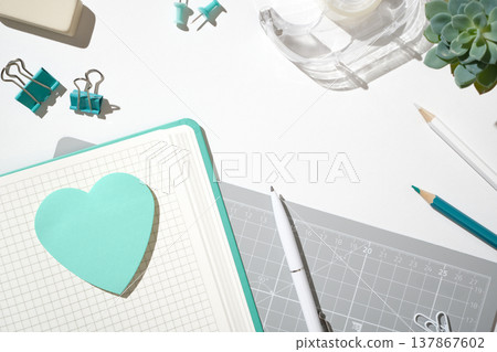 Notebook with a turquoise heart sticker on a grey cutting mat. Creative workspace for office and craft projects. Copyspace 137867602