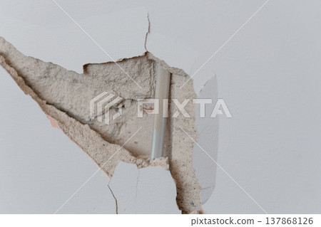 Damaged White Wall With Cracked Plaster Revealing Insulation And Pipe Inside Showing Structural Repair Needs In Neutral Tones Damaged White Wall With Cracked Plaster Revealing Insulation And Pipe Inside Showing Structural Repair Needs In Neutral Tones 137868126