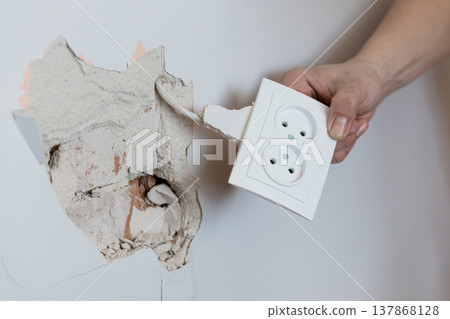 Electrician Removing Broken White Wall Socket Exposing Cracked Plaster and Electrical Wiring in Home Renovation Scene With Realistic Detail Electrician Removing Broken White Wall Socket Exposing Cracked Plaster and Electrical Wiring in Home Renovation Scene With Realistic Detail 137868128