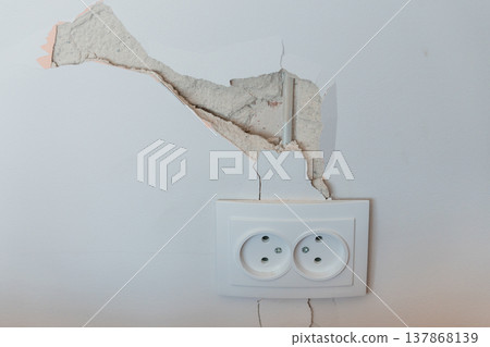 Damaged White Wall With Cracked Plaster Above Double European Electrical Outlet Showing Exposed Concrete And Vertical Fracture Lines In Realistic Style 137868139